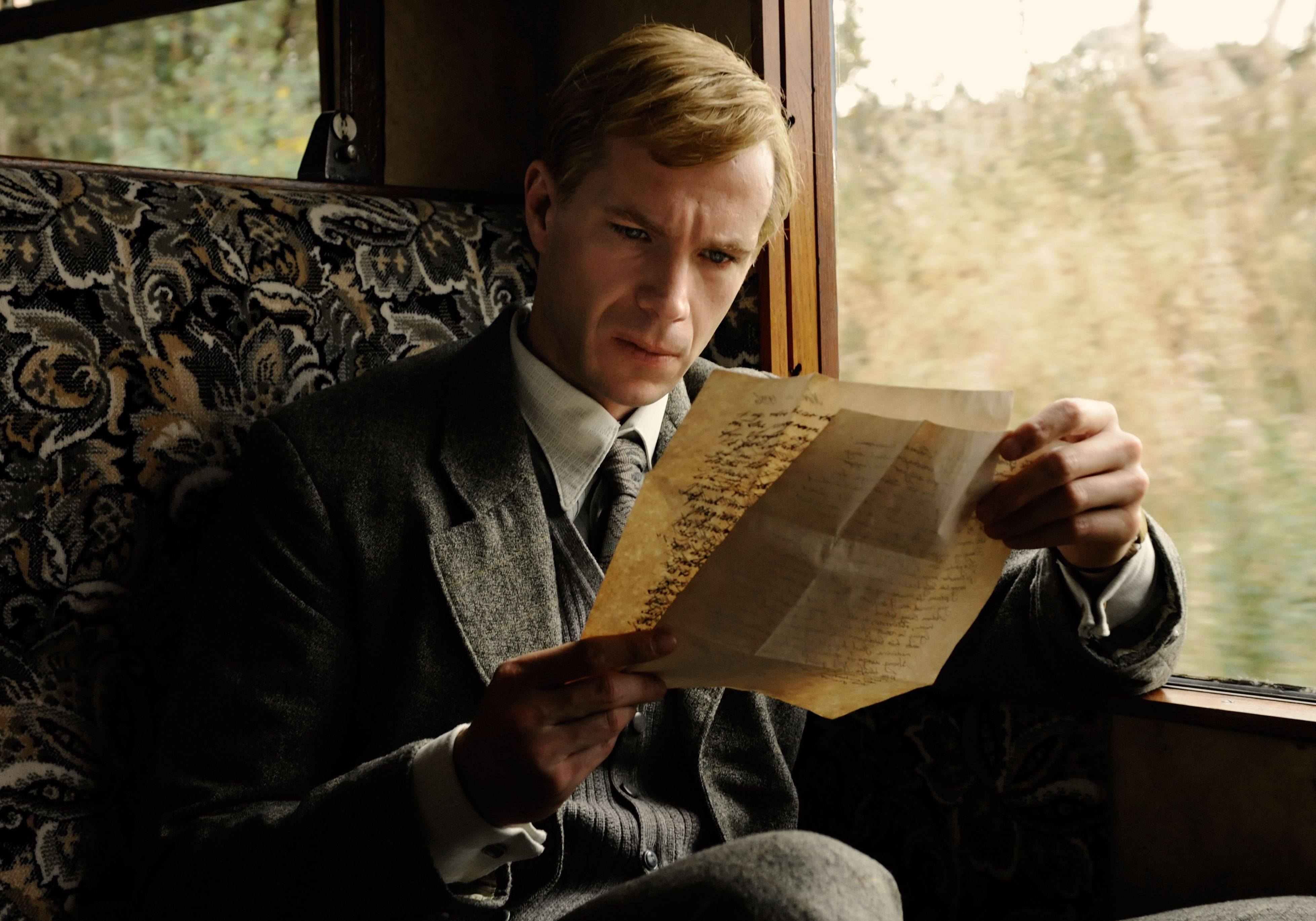 Blond James D&#039;Arcy inspects an old document in Cloud Atlas